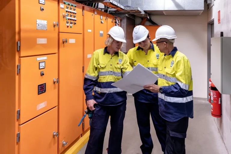 Engineers discussing plans in front of electrical panels.